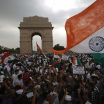 Large crowd of protesters waving Indian national flags at India Gate, New Delhi, during a public demonstration