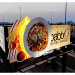 3D highway billboard advertising an Italian restaurant featuring an oversized plate of spaghetti with meatballs and illuminated pasta elements extending beyond the billboard.