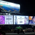 Multiple illuminated billboards at night in Indian city featuring retail, jewelry, and real estate outdoor advertising campaigns
