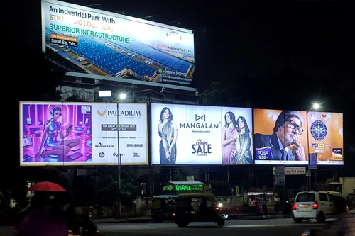 Multiple illuminated billboards at night in Indian city featuring retail, jewelry, and real estate outdoor advertising campaigns