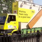 A branded outdoor mobile van advertising campaign by Idea features a bright yellow promotional vehicle with large billboard-style panels and bold messaging supporting Team India. The mobile advertising truck is designed for high visibility roadshows, outdoor brand promotions, and citywide marketing activations targeting mass public engagement.