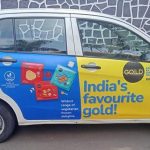 A cab branding campaign features a fully wrapped car advertisement promoting a frozen food brand with colorful vehicle graphics and bold product messaging. The transit advertising setup uses branded taxi wraps and mobile outdoor advertising to increase brand visibility across busy city roads and urban locations.