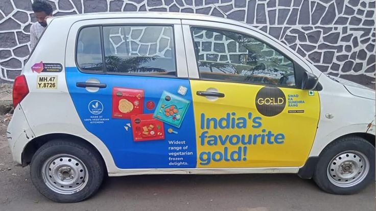 A cab branding campaign features a fully wrapped car advertisement promoting a frozen food brand with colorful vehicle graphics and bold product messaging. The transit advertising setup uses branded taxi wraps and mobile outdoor advertising to increase brand visibility across busy city roads and urban locations.