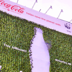 A sustainable outdoor advertising campaign by Coca-Cola and WWF featuring a large eco-friendly billboard covered with live green plants shaped around a Coca-Cola bottle silhouette. The campaign promotes environmental awareness and air pollution reduction, showcasing how sustainable outdoor advertising in India uses green installations and eco-conscious branding to build consumer trust and environmental responsibility.