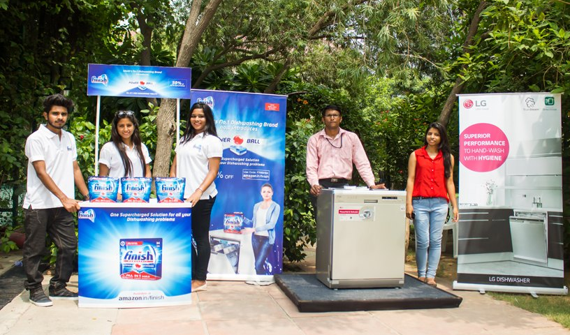 An outdoor product demonstration and experiential marketing setup by Finish and LG showcases a dishwasher activation campaign with brand promoters, display kiosks, and live product interaction in an open public space. The activation combines on-ground engagement, product education, and face-to-face brand interaction to demonstrate dishwasher benefits and hygiene-focused cleaning solutions.