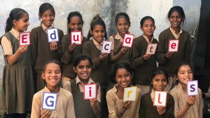 This image shows a group of young school girls holding a paper which says Educate Girls as a part of marketing campaign of Starbucks