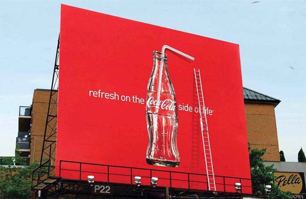 An innovative 3D coca cola billboard featuring a glass bottle of coke, a straw and a ladder.

