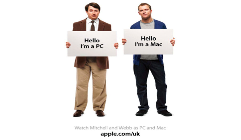 Watch Mitchell holding the “Hello, I am a PC” placard accompanied by Webb holding the “Hello, I’m a Mac” placard.