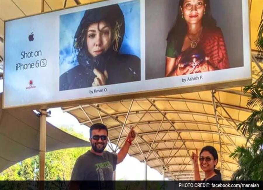 A couple posing with an Apple billboard.
