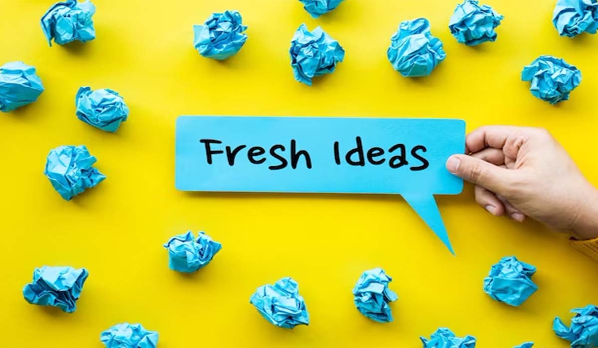 A yellow background with crumpled blue papers and a hand featuring a dialogue box “Fresh ideas”.

