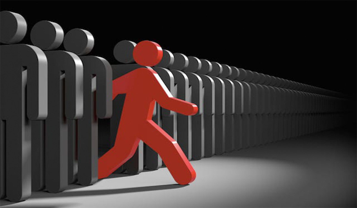 A red human-like figure walking out from the crowd of black people.
