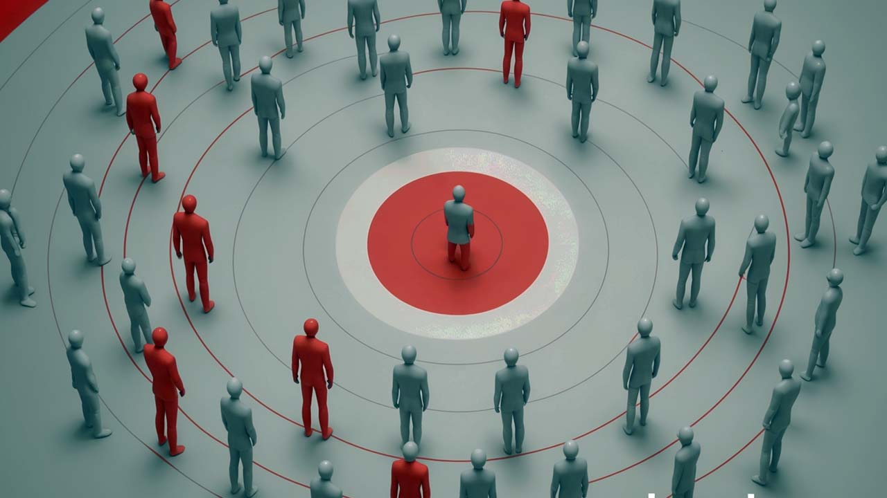 A picture featuring various grey-coloured human-like figures and only one red human figure within a target circle.
