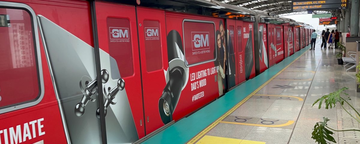 Red metro train fully wrapped with GM LED lighting advertisement at an elevated metro station platform.