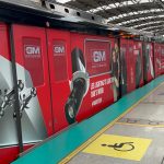 Red metro train fully wrapped with GM LED lighting advertisement at an elevated metro station platform.