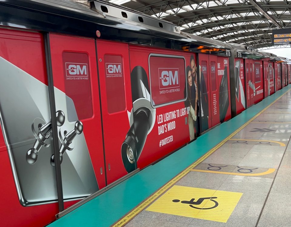 Red metro train fully wrapped with GM LED lighting advertisement at an elevated metro station platform.