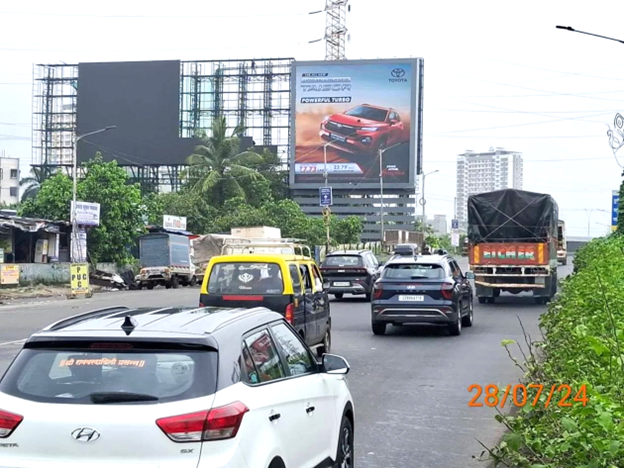 Automotive brand hoarding on a busy suburban Mumbai road with continuous car and truck traffic.