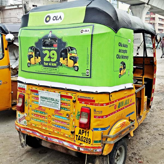 Ola advertisement displayed on the back of an auto rickshaw in city traffic