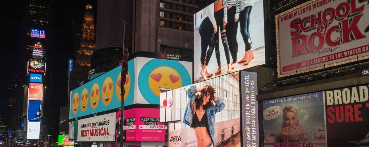 Nighttime view of Times Square filled with illuminated digital billboards promoting Broadway shows, fashion brands, and entertainment campaigns.