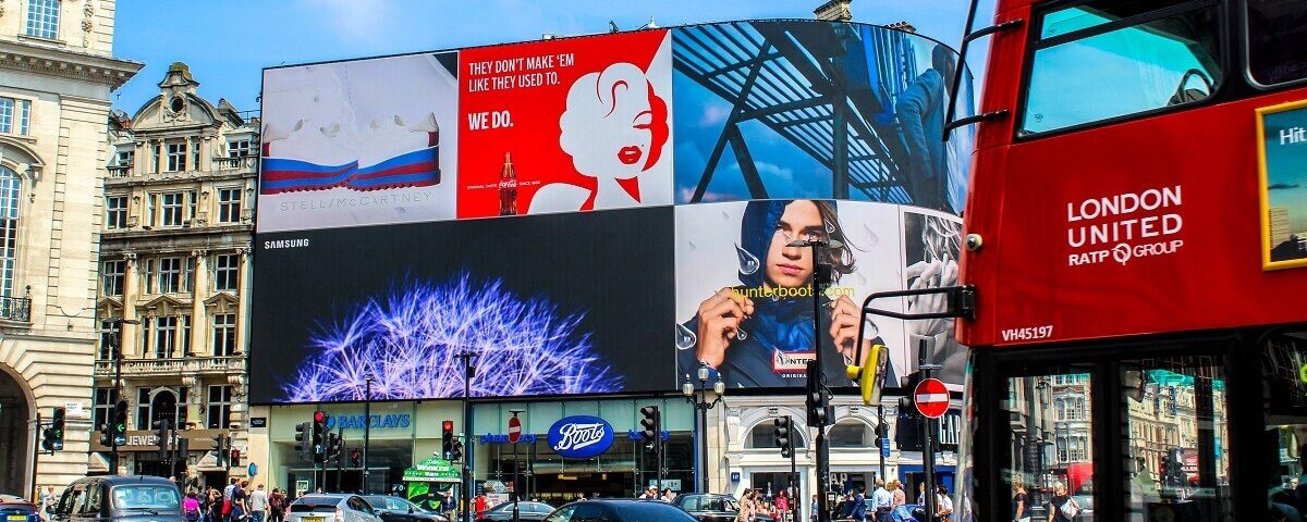 Large digital billboards displaying multiple brand advertisements at a busy city intersection with traffic and pedestrians visible