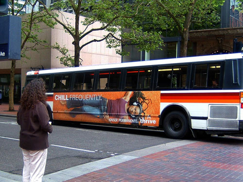 City bus wrapped with a Kaiser Permanente health campaign advertisement reading “Chill Frequently,” parked at an urban intersection.