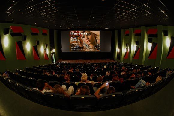 Cinema hall with seated audience watching a large movie screen displaying a commercial advertisement before the film.
