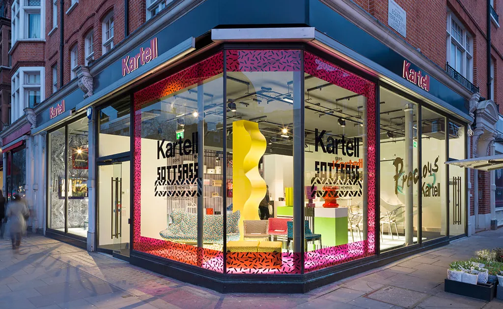 Kartell Experiential Retail Window Display and Branded Storefront Activation Kartell retail storefront with illuminated window display and bold pink graphic framing at a street corner.