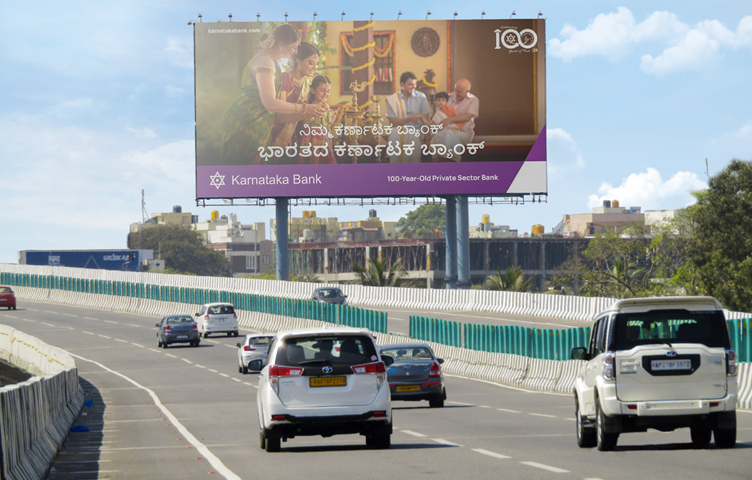 Karnataka Bank roadside billboard displayed along a highway with moving traffic