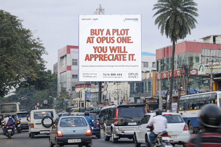 Real estate billboard reading “Buy a plot at Opus One” above city traffic