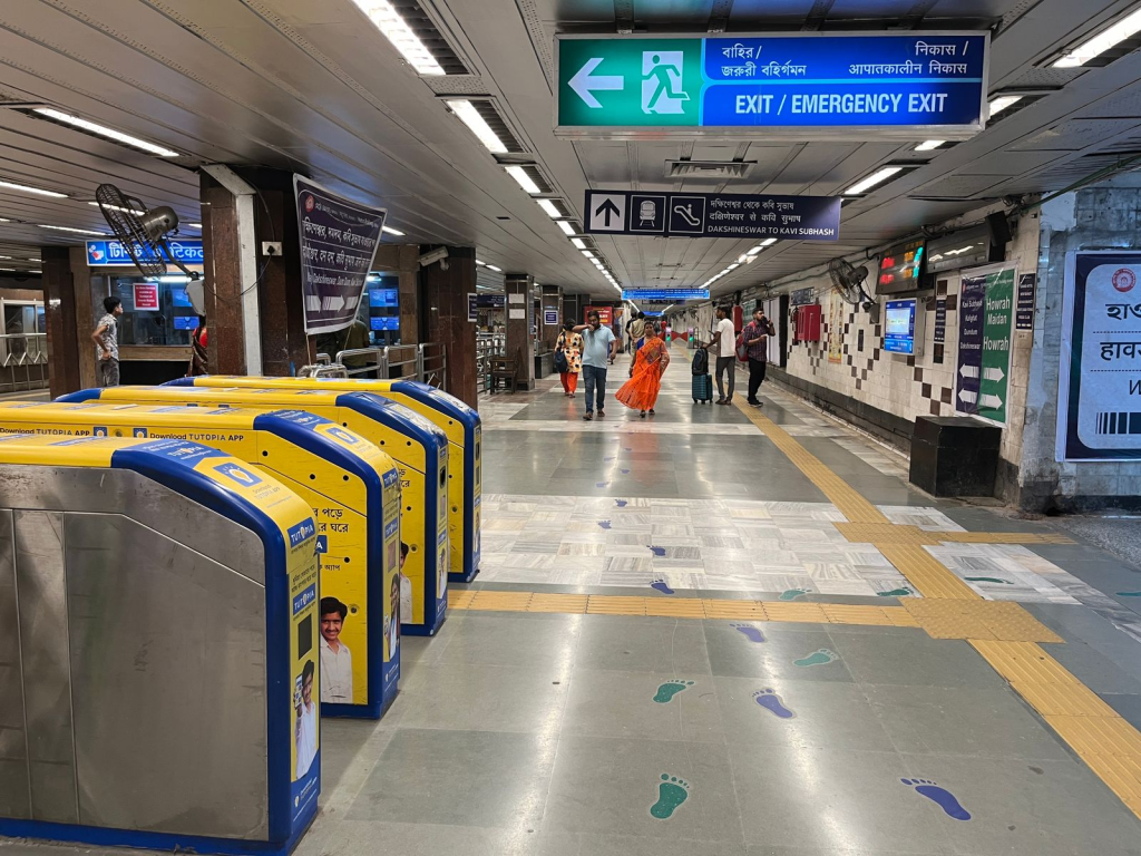 Metro station concourse with ticket gates, floor markings and multiple advertising panels