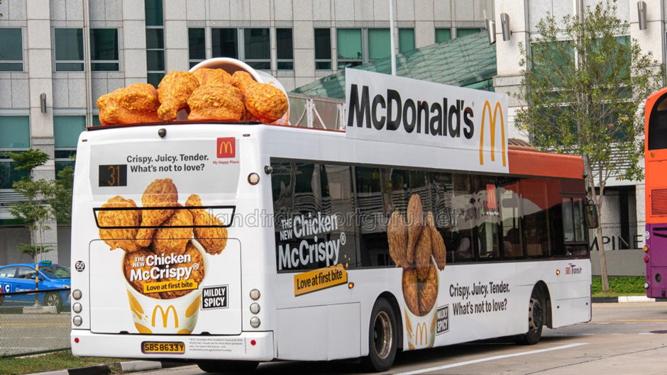 McDonald’s bus wrapped with Chicken McCrispy promotion featuring large fried chicken visuals and branding on a city street.
