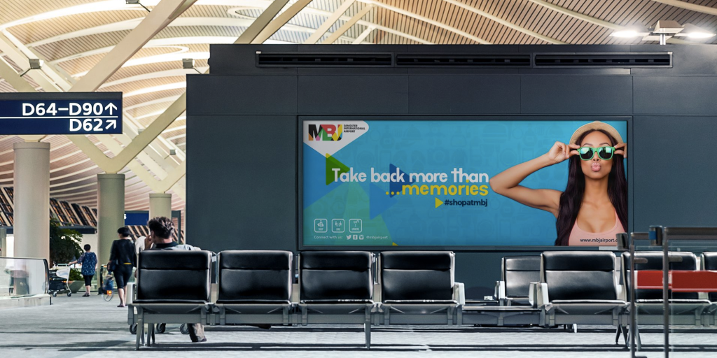 Airport waiting area with digital billboard reading “Take back more than memories” and a woman wearing sunglasses promoting airport shopping.