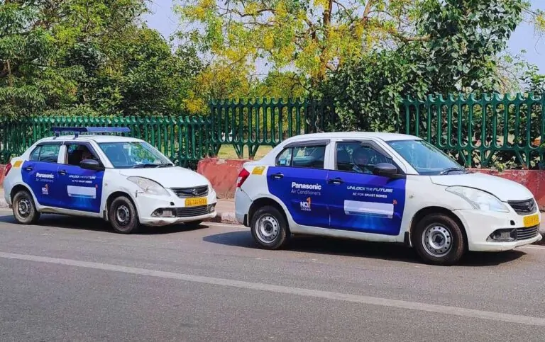 Two taxis parked roadside featuring Panasonic air conditioning branding on vehicle doors in an urban area.