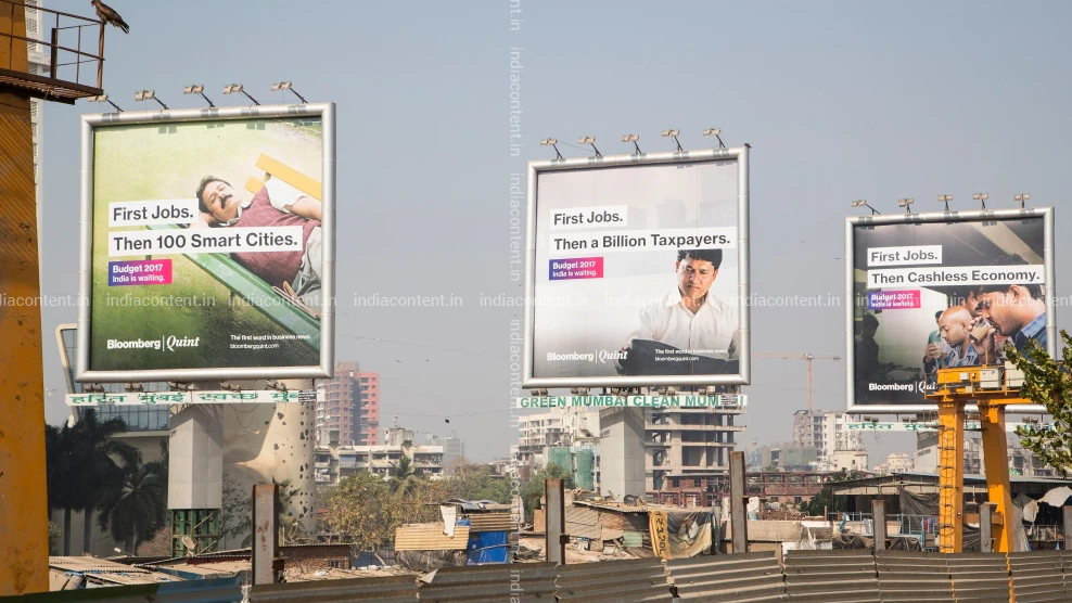 Three elevated billboards promoting Bloomberg Quint’s Budget messaging positioned above an urban landscape with ongoing construction and city infrastructure.