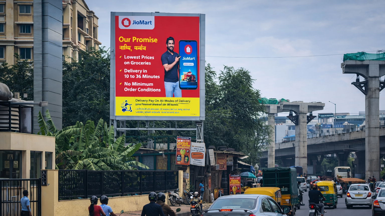 JioMart promotional billboard placed along a city road near residential buildings and a metro line, with two-wheelers and cars passing by.