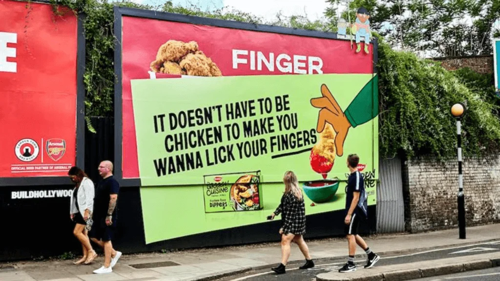 Large roadside billboard with creative copy and fried chicken visuals designed to attract attention from pedestrians walking by.