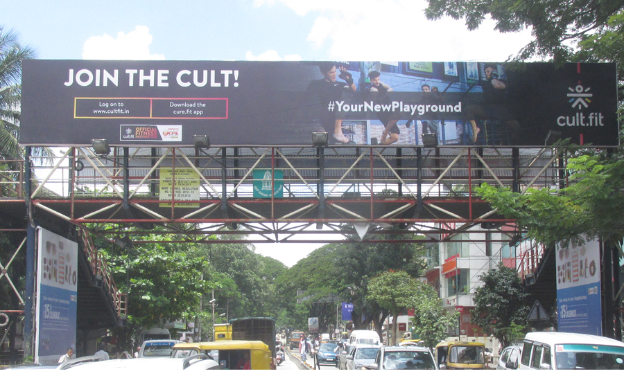 Large billboard on a flyover promoting Cult.fit fitness app with traffic moving below in a busy urban setting.
