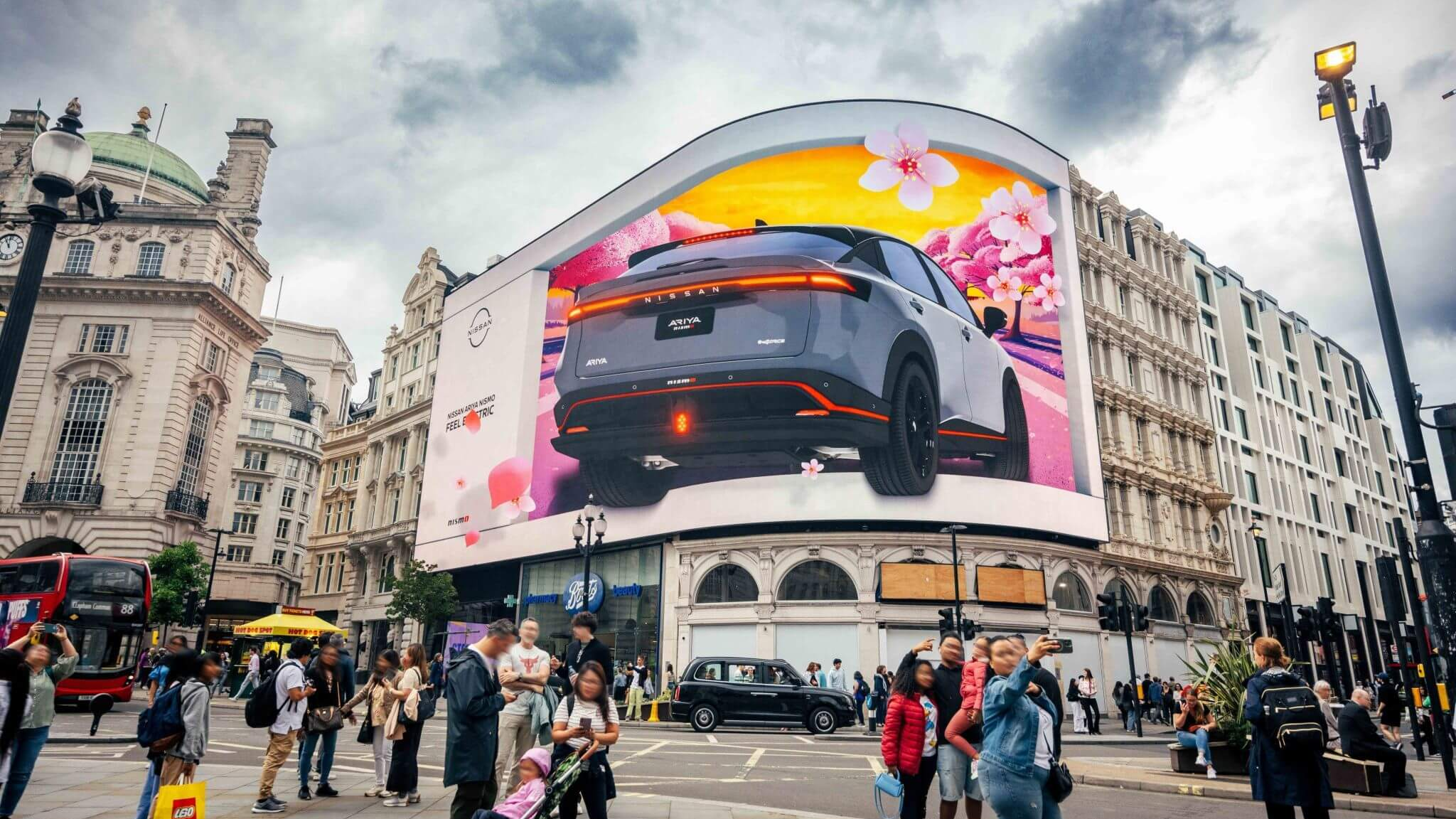 Large curved digital billboard displaying a car advertisement in a busy urban intersection with pedestrians