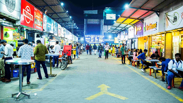Busy street food market with multiple food stalls and customers dining in urban night setting