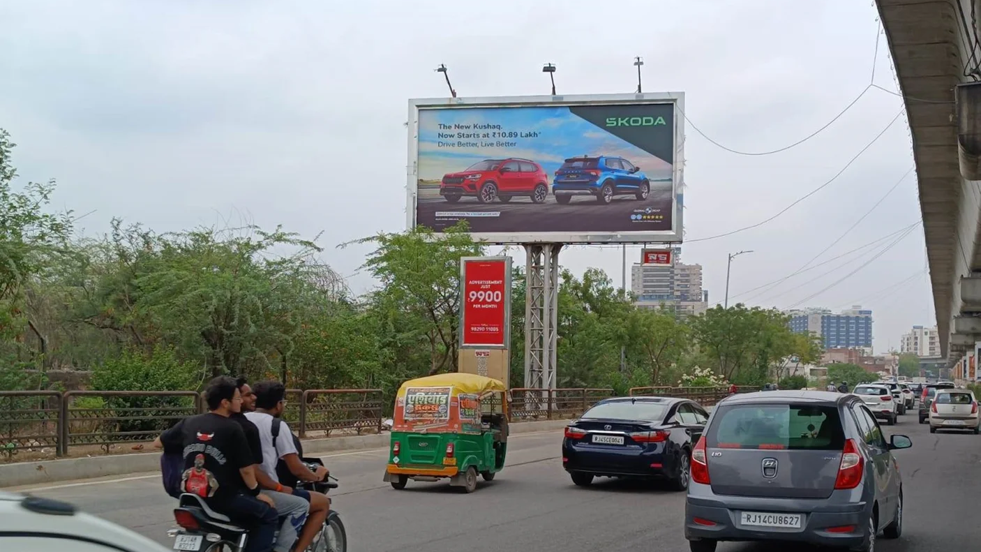 Skoda car billboard showcasing SUV models placed above city road with vehicles and metro line