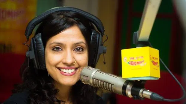 Female radio host wearing headphones speaking into a studio microphone during a live broadcast at a radio station.