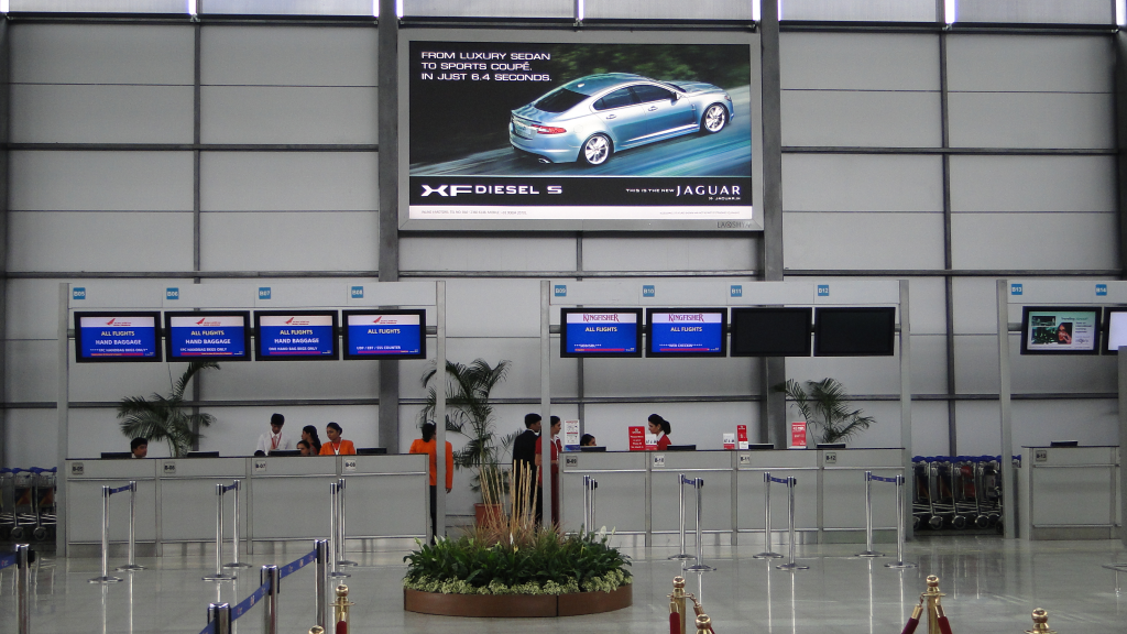 Airport check-in counters with a large overhead billboard advertising the Jaguar XF Diesel S car above airline service desks.