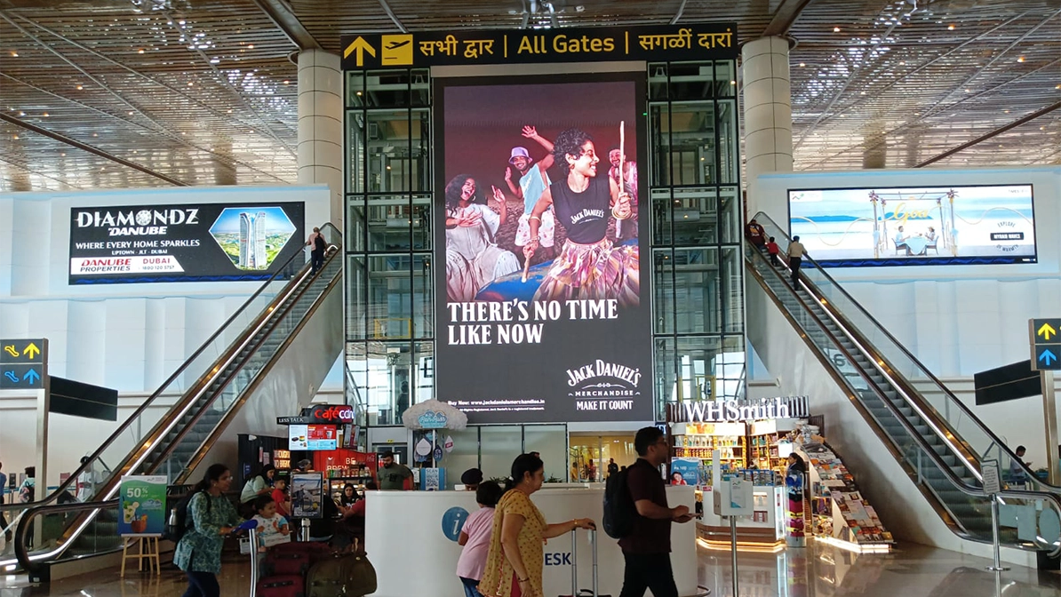Large vertical advertising screen for Jack Daniel’s whiskey placed between escalators in a busy airport terminal atrium.
