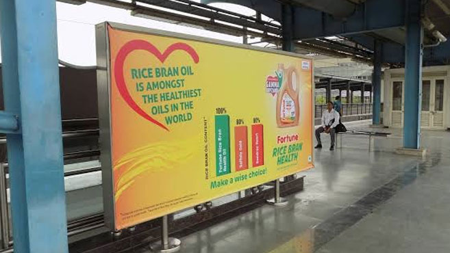 Railway platform billboard promoting Fortune rice bran oil with health benefits messaging and product visuals