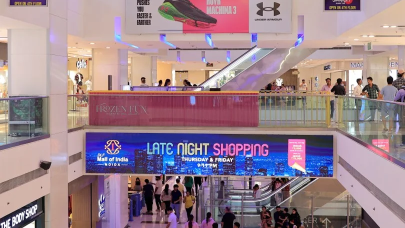 Shopping mall interior with large banner promoting late night shopping and people walking across floors