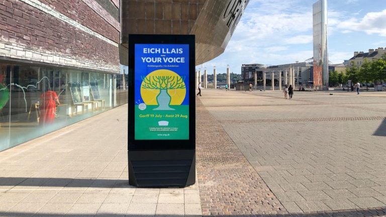Vertical digital billboard in an open urban plaza with colorful event advertisement design