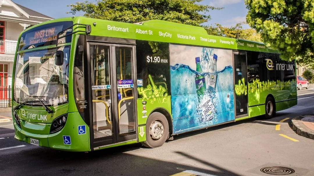 Green city bus wrapped with beverage advertisement driving through a residential street