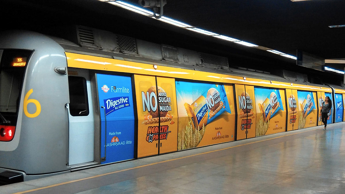 Metro train wrapped with bright food brand advertising inside an underground station platform
