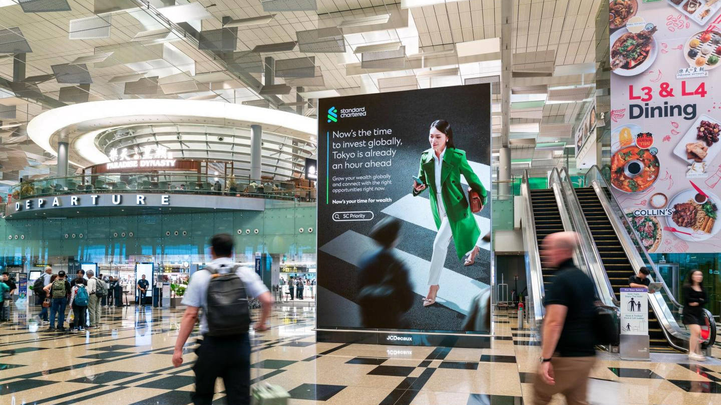 Airport terminal with large digital advertising display near departure area and travelers walking