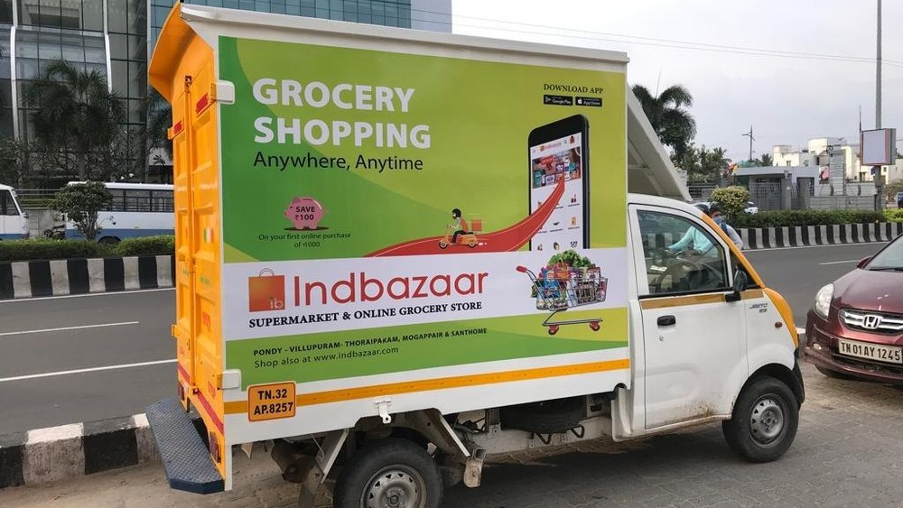 Small delivery truck with Indbazaar grocery advertisement parked roadside in an urban area