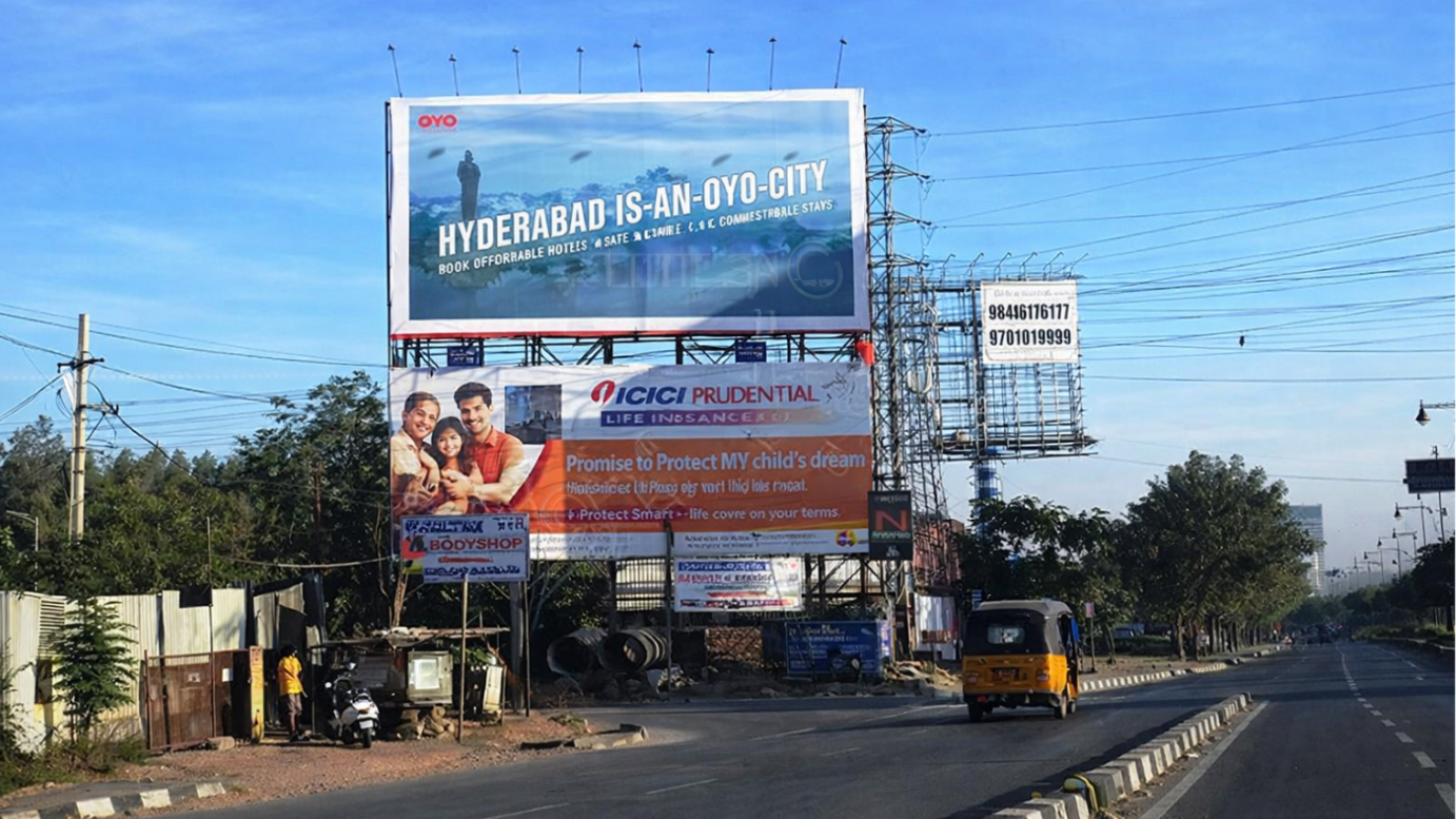 A view of a city road featuring stacked billboards for OYO and ICICI Prudential. A yellow auto-rickshaw travels along the sunlit, tree-lined asphalt road.